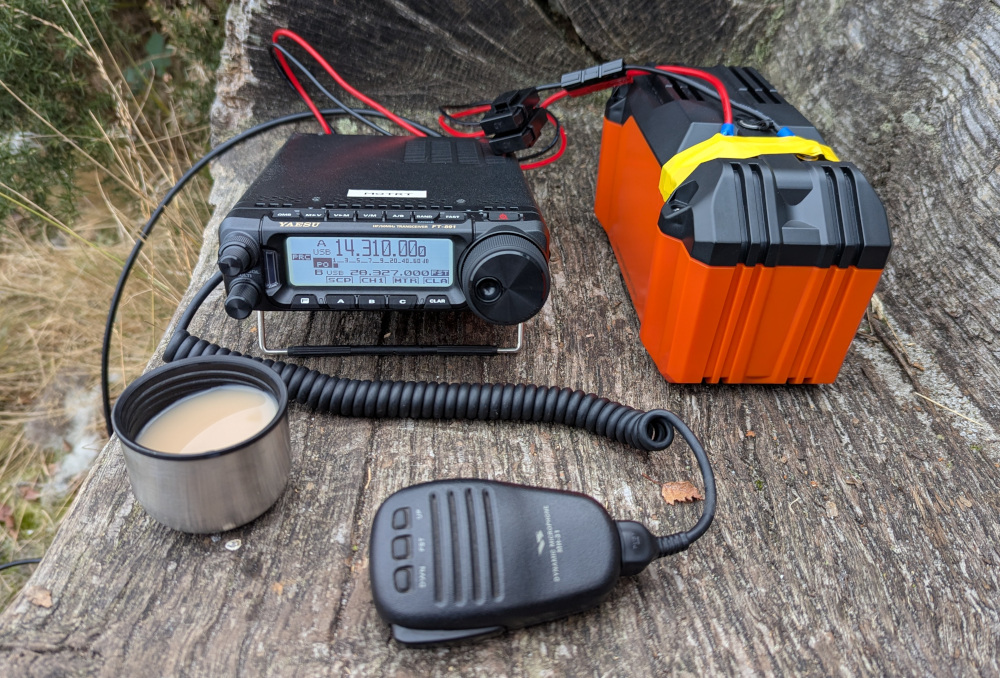 A radio, battery and cup of tea set up on a wooden bench