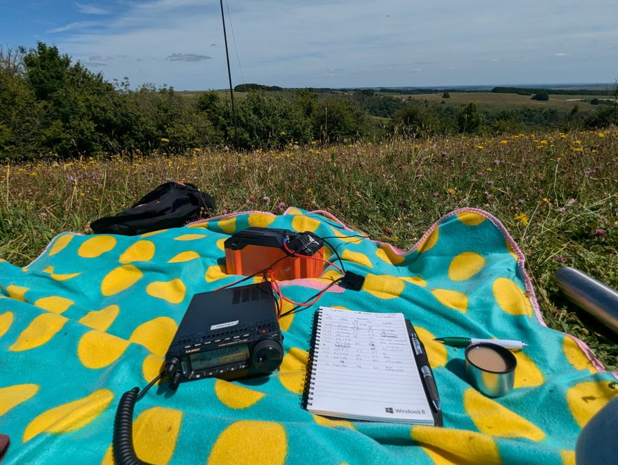 Picnic blanket with radio, battery, paper log and cup of tea