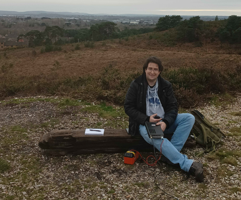 Me sat on a plank of wood with radio in hand, view of Poole behind me