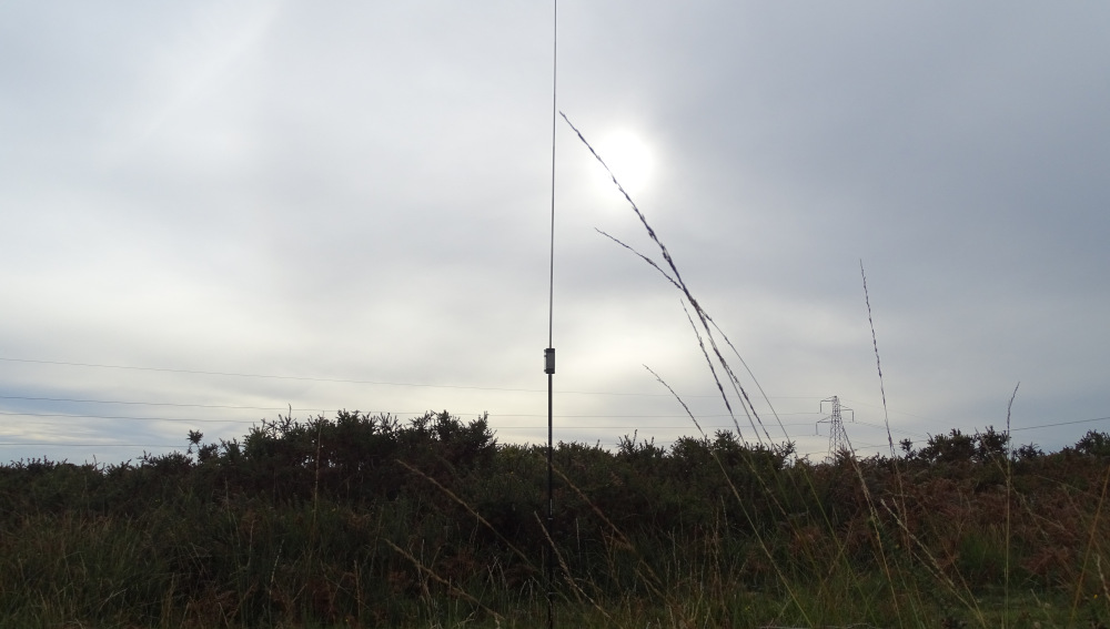 JPC-12 antenna with loading coil silhouetted against a faint sun in a cloudy sky