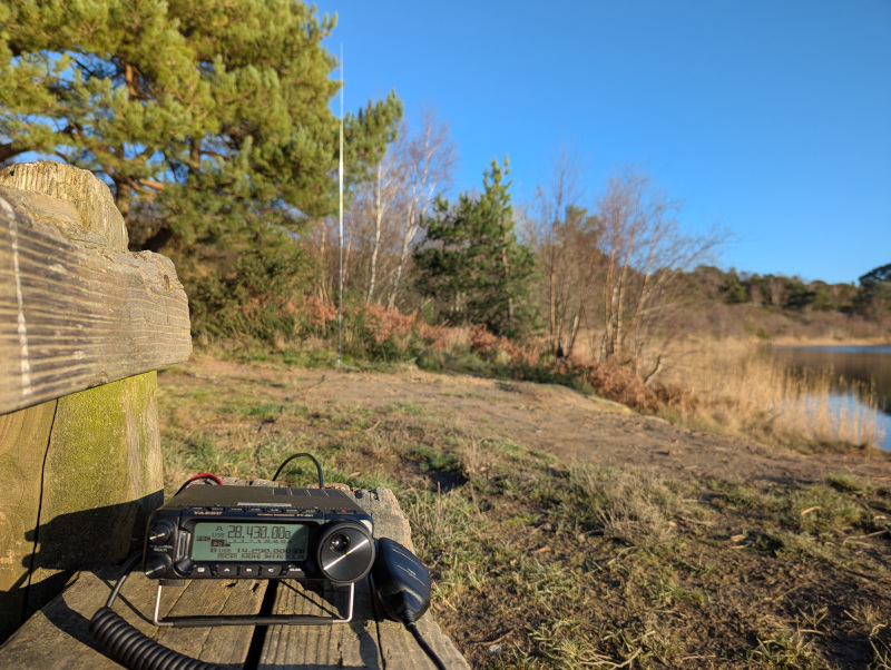 A radio on a wooden bench, antenna out of focus in the background