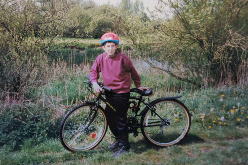 Me at age 9-10, stood with my bike on a patch of grass with the river in the background