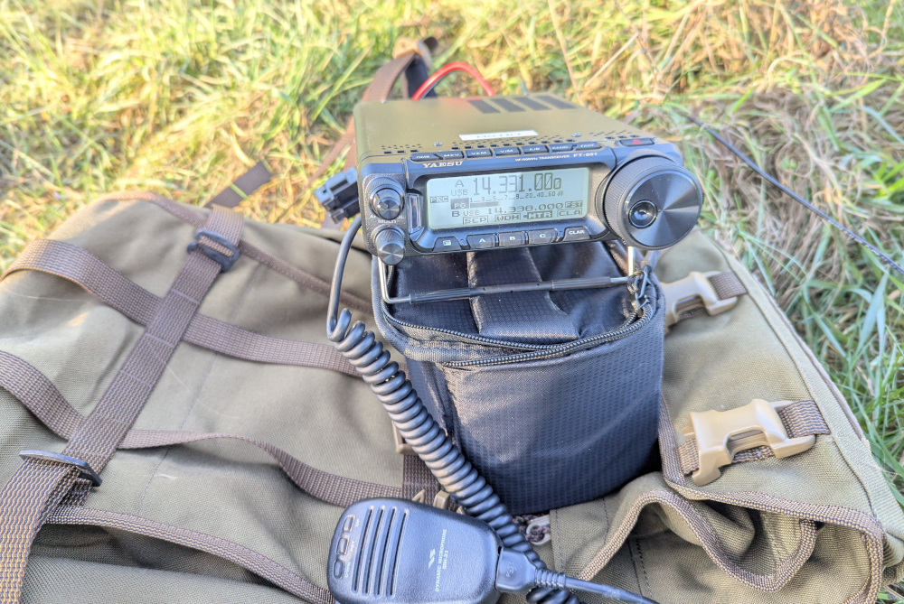 A brown backpack and black battery pouch make a tower of stuff on which sits the radio