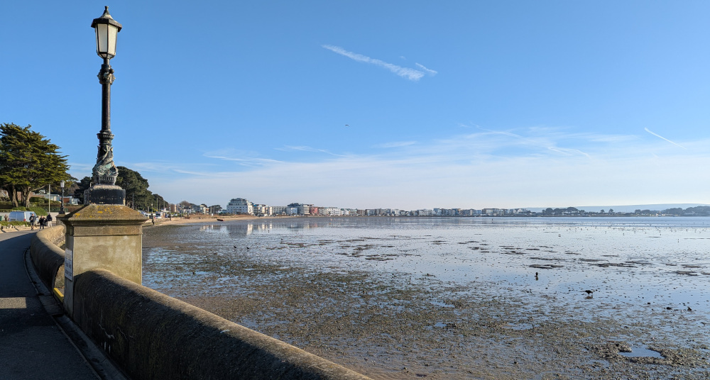 A harbour at low tide, with mud in the foreground, framed by a pavement with an old-fashioned looking streetlamp