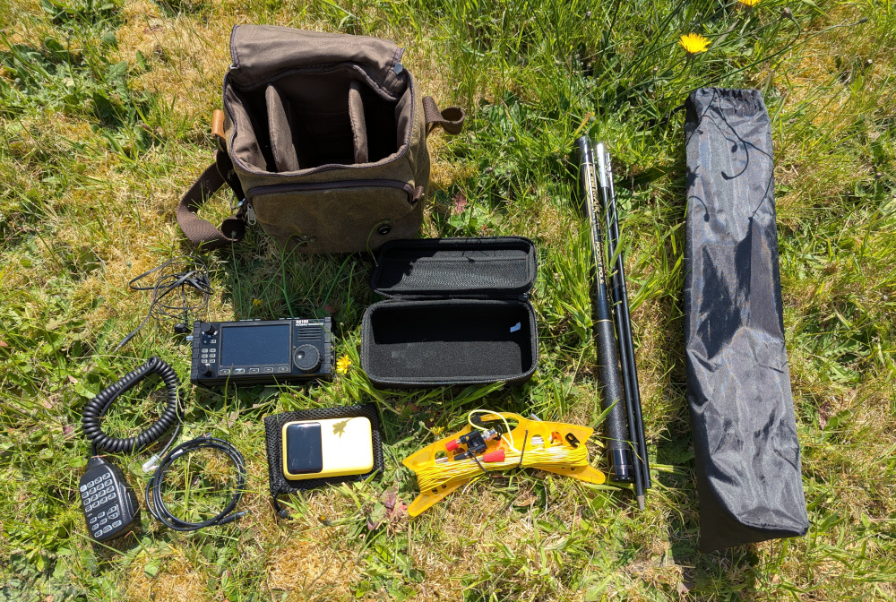 A bag with a number of radio items unpacked and displayed alongside it on the grass