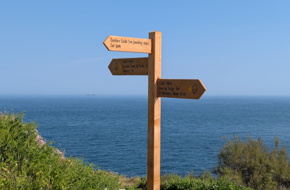 Photo of a signpost with bushes in the foreground and the sea in the background