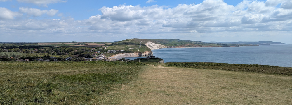 View down a long green hill, with Freshwater Bay in the background