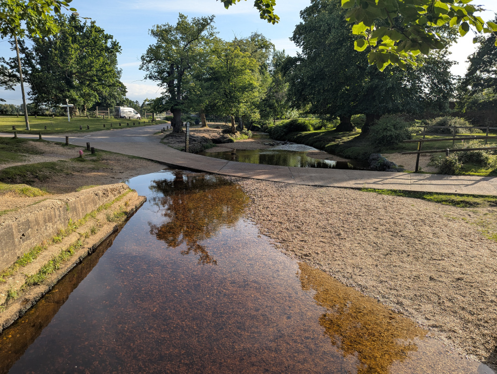 A small rust-red stream flowing underneath a ford. The water level is so low that the ford is completely above the water level.