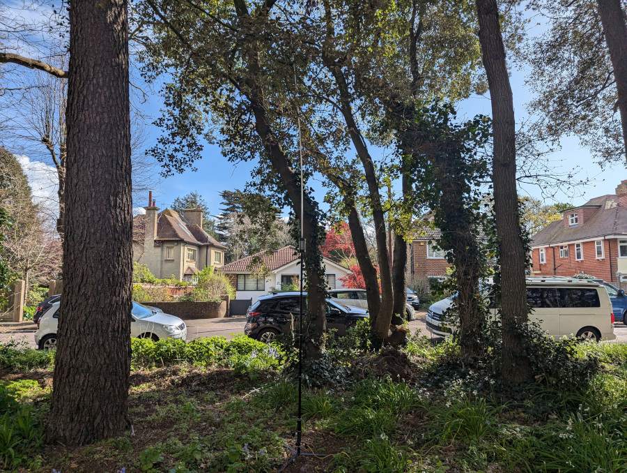 JPC-12 vertical antenna with a car-lined road in the background, and some greenery around