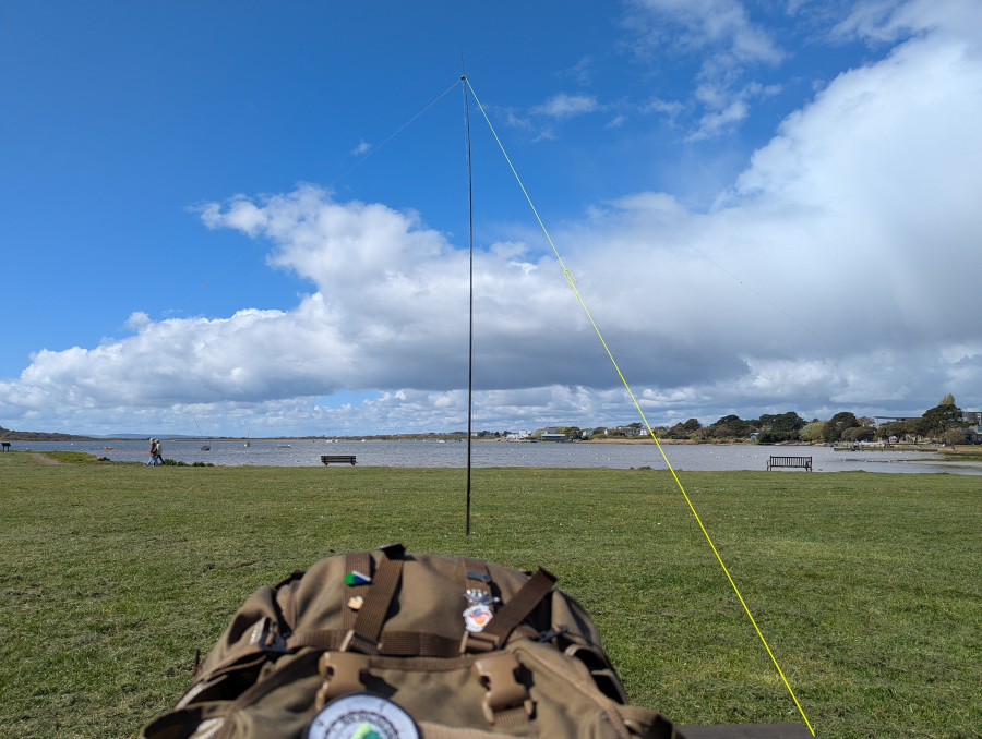 Inverted-V dipole antenna on an area of cut grass. In the background is a shallow and muddy harbour. The sun is shining and the sky is blue.