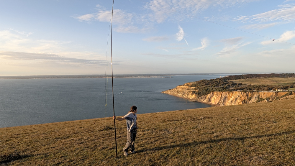 Inverted V dipole antenna held up by logging assistant, staring off to Alum Bay in the distance