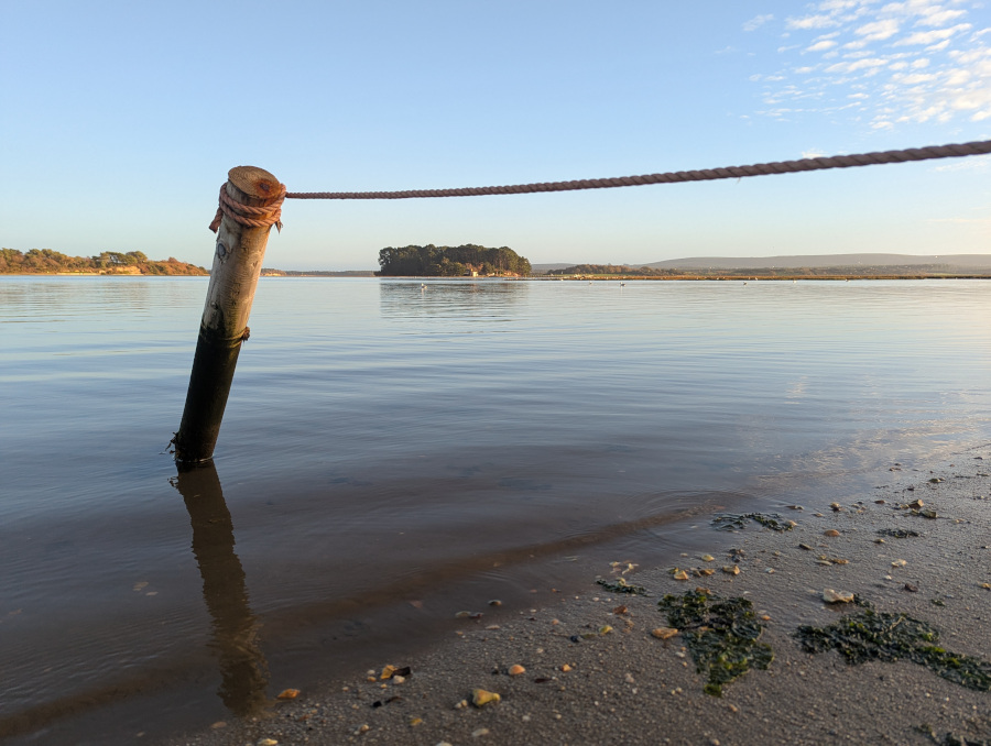View of a flat calm sea and sky, framed by a post and rope