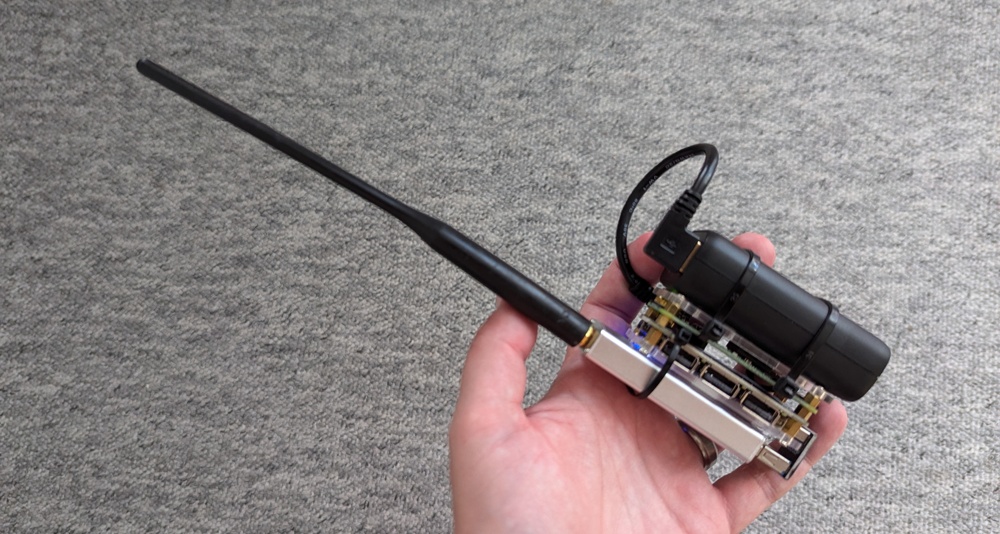 A Raspberry Pi Zero W, USB pHAT, RTL-SDR dongle, antenna and battery attached together, held in a hand